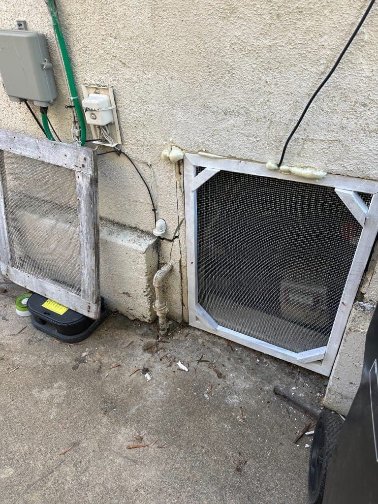 Crawl space vent fitted with new metal screening beside an exterior bait station